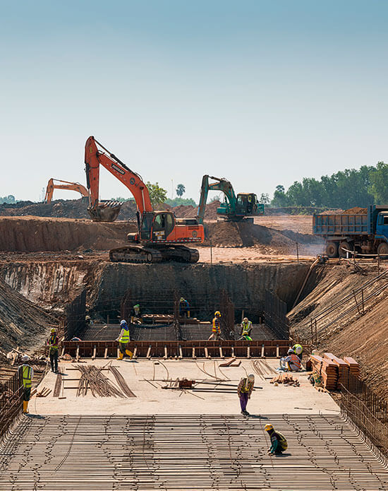 Homens trabalhando em uma construção com duas retroescavadeiras e um caminhão