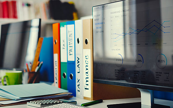 Foto de uma mesa de escritório com dois monitores e pastas de databook